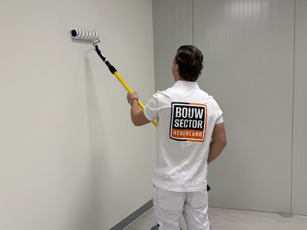 Schilder met roller aan een verlengsteel werkt een witte wand af tot tegen de hoek