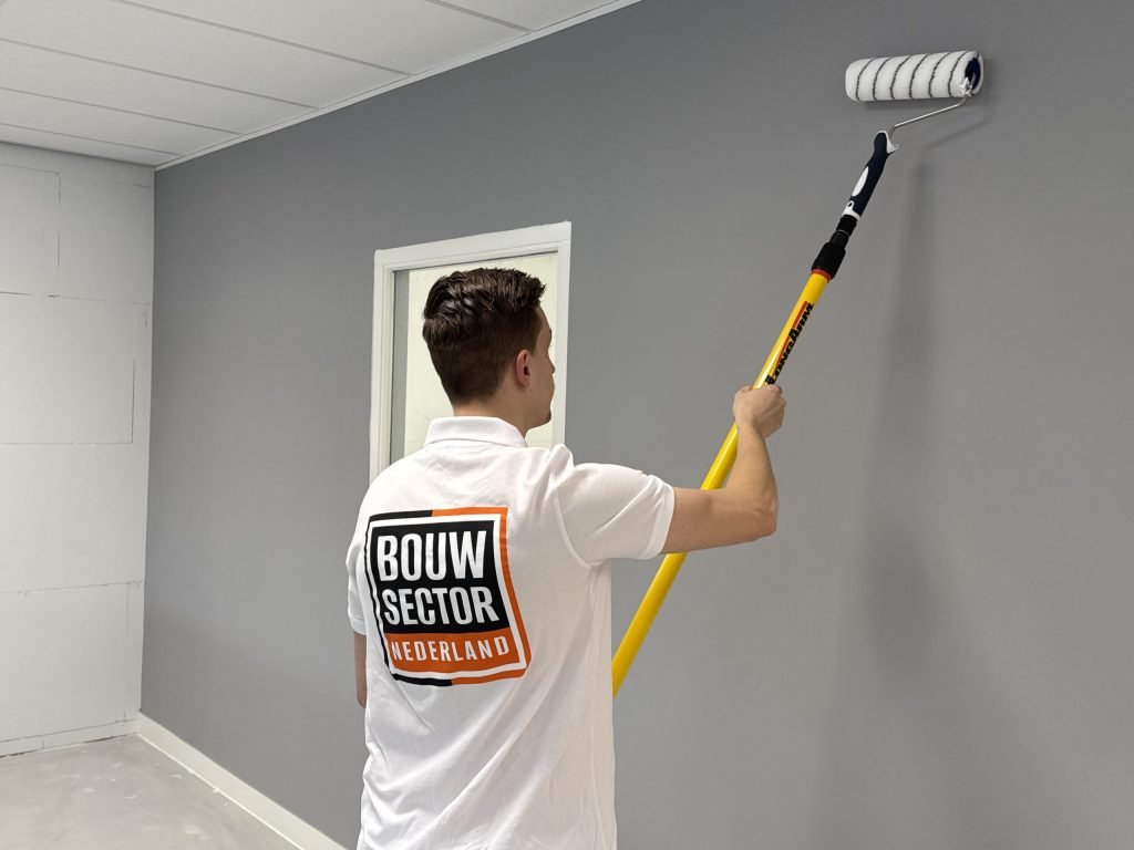 Schilder zet een grijze wand met de roller in een ruimte met een plafond van platen