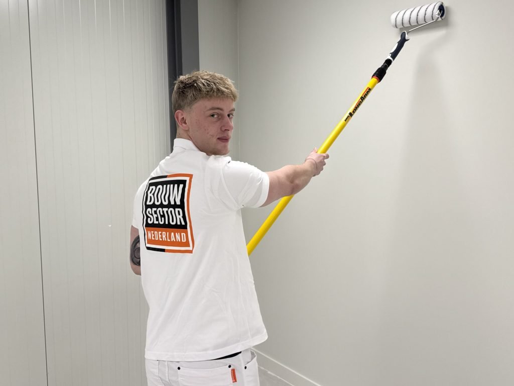 Schilder kijkt over zijn schouder terwijl hij de bovenkant van een witte wand rolt