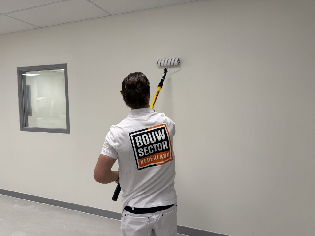 Schilder van Bouwsector Nederland zet met een roller op een verlengsteel een lichte wand in de verf